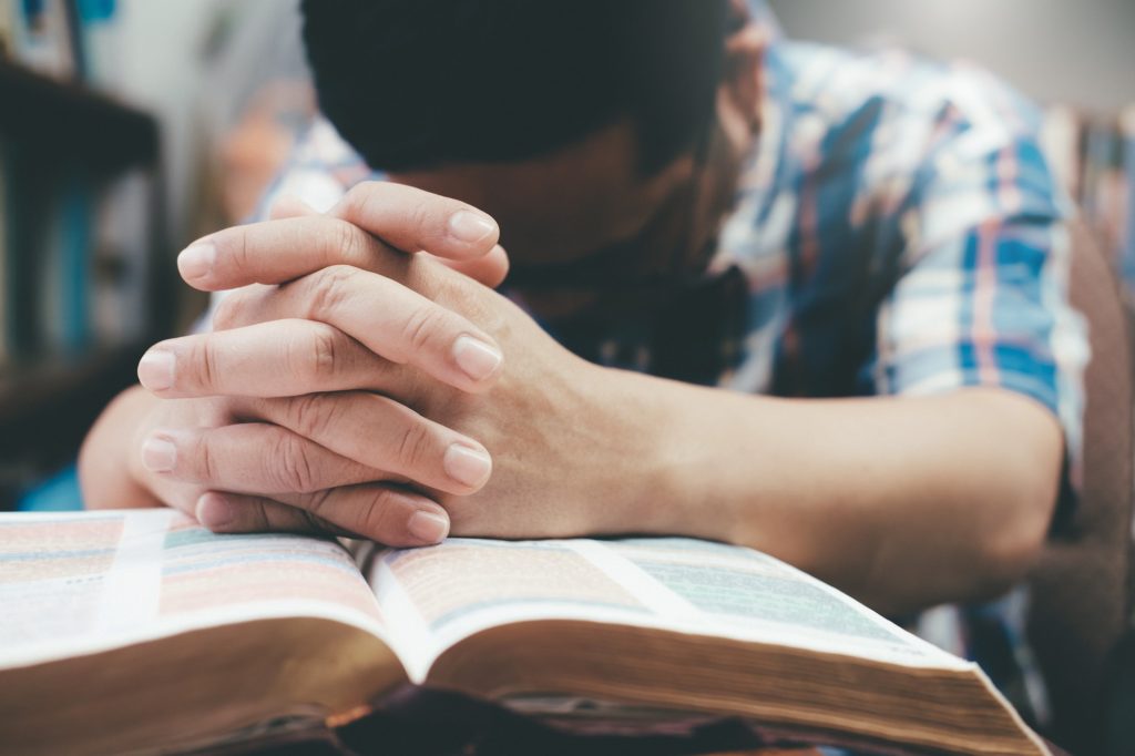 Man praying, hands clasped together on his Bible.